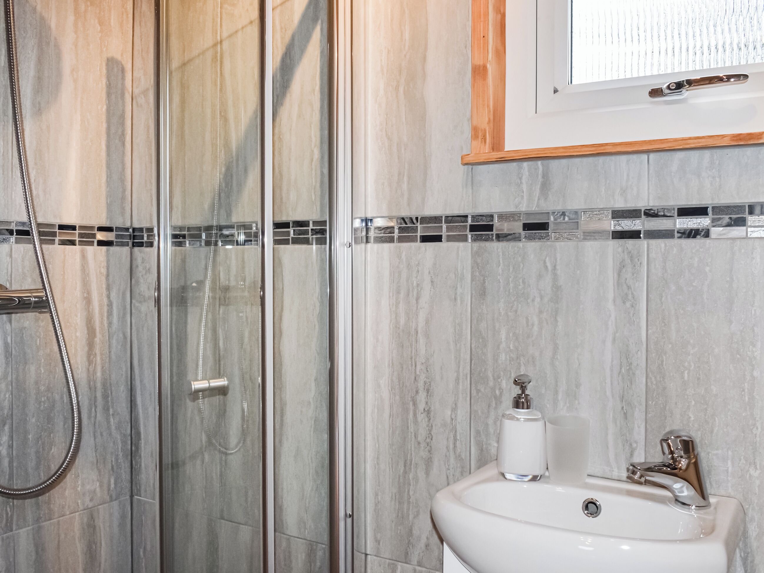 A bathroom with a glass shower enclosure, a sink with a chrome faucet, and a mirror above the sink.