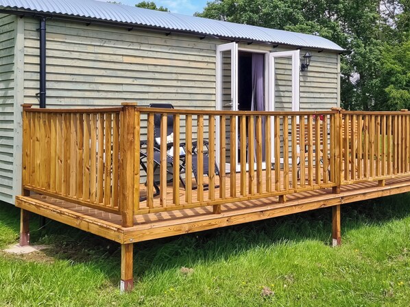 A wooden deck attached to a building with a metal roof and a door open.
