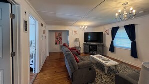 Een woonkamer met een grijze bank, een salontafel, een televisie en een kroonluchter.