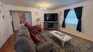 Een woonkamer met een grijze bank, rode kussens, een televisie en een vloerkleed met dessin.