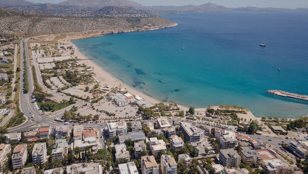 Vista aérea de un pueblo costero con playa, aguas azules cristalinas y una combinación de edificios residenciales y comerciales.