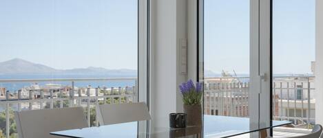 A balcony with a glass table and chairs, a potted plant, and a view of a cityscape and mountains.