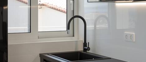 A modern kitchen with a black faucet, white tiles, and a window overlooking a red-tiled roof.