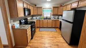 A kitchen with wooden cabinets, a black refrigerator, a stove, and a microwave. - Enjoy this spacious ranch-style house next to the quilting capital of the world. (Hamilton)