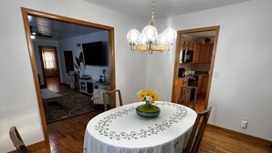 A dining area with a round table, chairs, a chandelier, and a view into the kitchen and living room. - Enjoy this spacious ranch-style house next to the quilting capital of the world. (Hamilton)