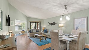 A spacious living room with a dining area, wooden floors, and a large window. - Updated Condo, Steps to Tennis + Pickleball Courts, Beach and Village, w/ a Pool (St. Simons Island)