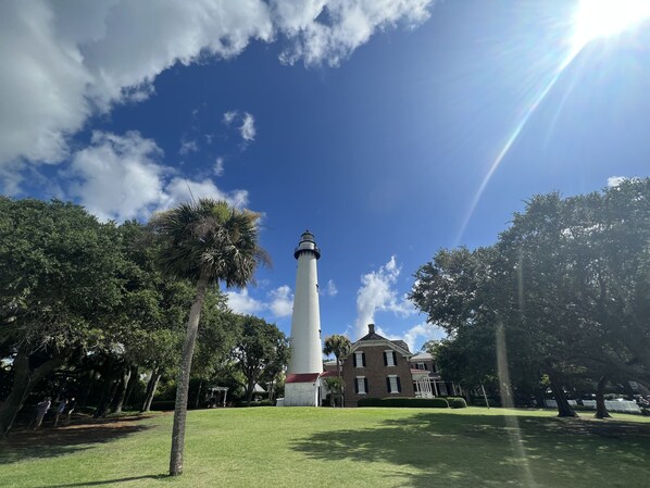 A lighthouse with a brick base and white tower, surrounded by trees and a building with a red roof.