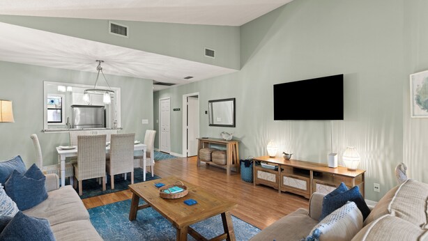 A spacious living room with a wooden coffee table, a sofa, and a TV mounted on the wall. - Updated Condo, Steps to Tennis + Pickleball Courts, Beach and Village, w/ a Pool (St. Simons Island)