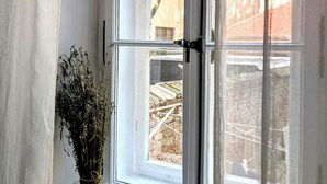 Une fenêtre avec des cadres blancs et une vue dégagée sur l’extérieur, notamment sur un arbre et un mur de briques.