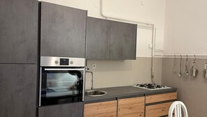 Une cuisine moderne avec des armoires grises, un four encastré, un évier et une cuisinière. On y trouve un plan de travail en bois et une chaise blanche près d’une table.