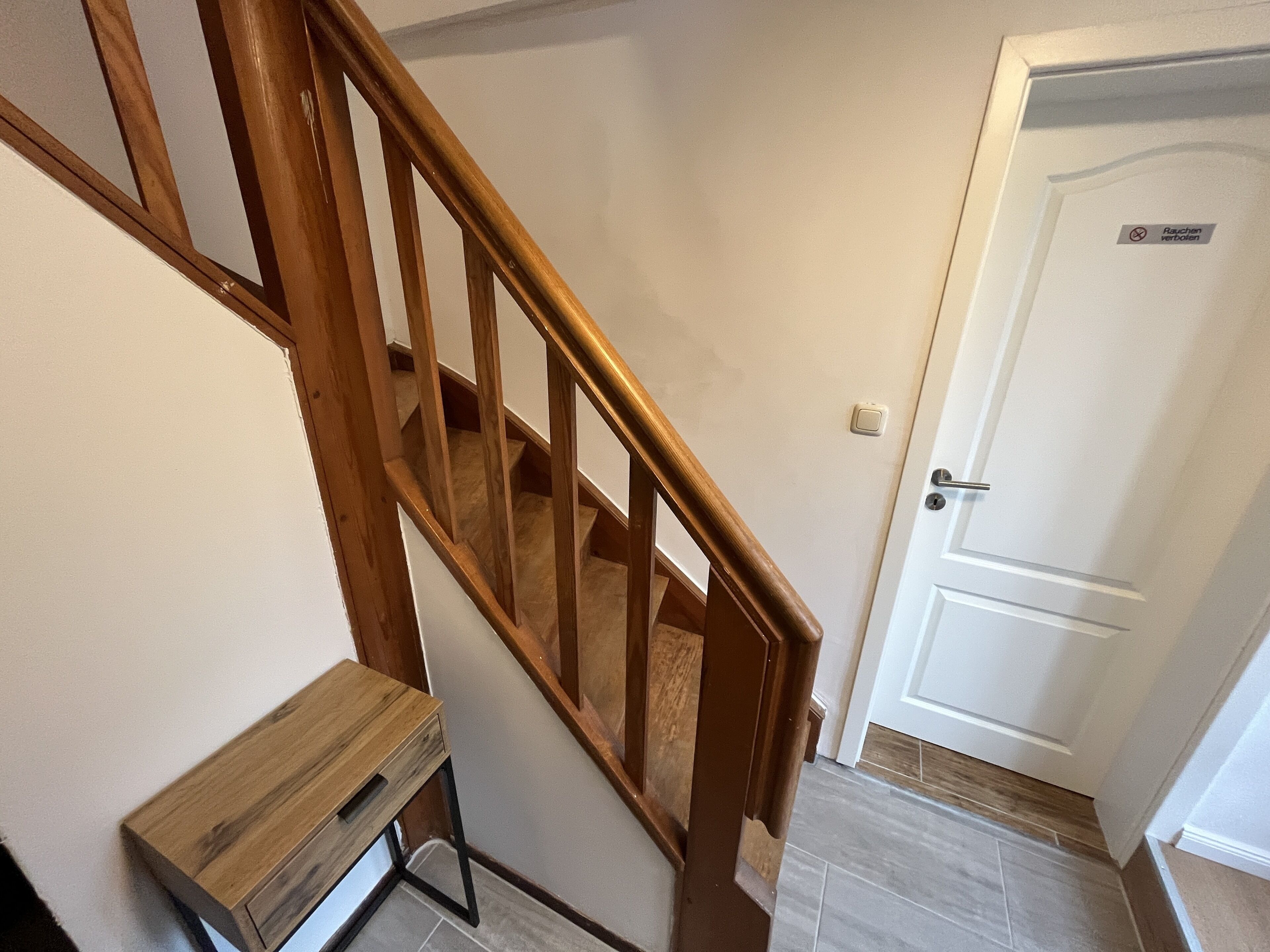 A wooden staircase with a handrail, a small wooden bench, and a white door with a sign.