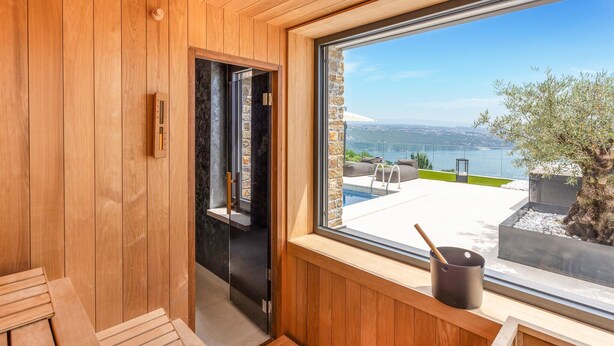A sauna room with wooden walls, a large window overlooking a pool and outdoor area, and a sauna tub. - Stunning home in Opatija with sauna (Opatija)