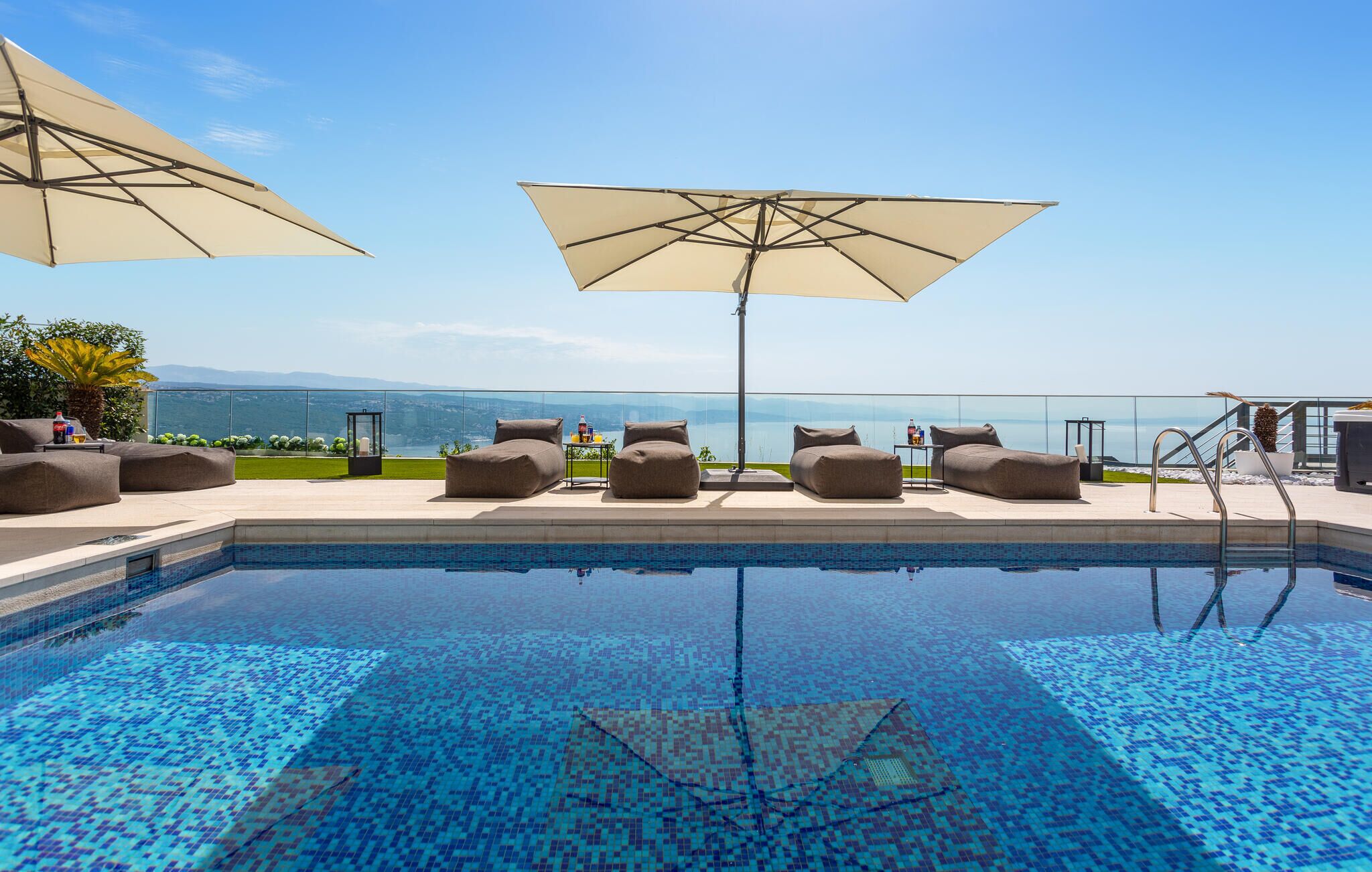 Ein Poolbereich mit Liegestühlen und Sonnenschirmen, mit freiem Blick auf das Meer und einem gefliesten Pool.