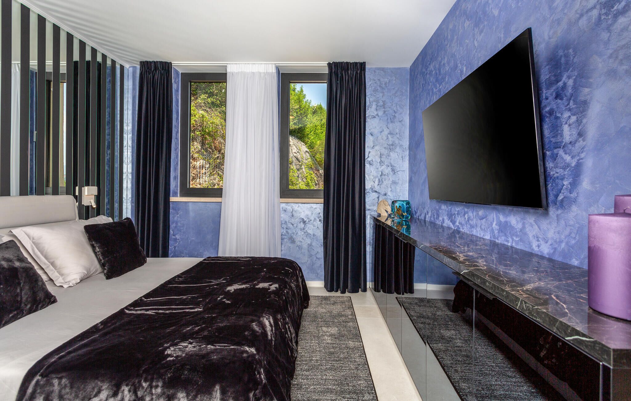 Um quarto moderno com uma cama, uma televisão e uma janela com cortinas.