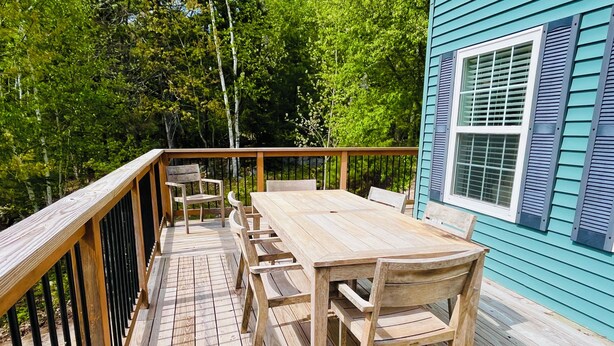 A wooden deck with a table and chairs, surrounded by a metal railing, and a house with blue siding and a window. - Acadia Retreat:18 Miles to Acadia NP!Secluded, Pet Friendly, Spacious. (Ellsworth)