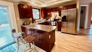 A modern kitchen with dark wood cabinets, stainless steel appliances, and a large island with bar stools. - Acadia Retreat:18 Miles to Acadia NP!Secluded, Pet Friendly, Spacious. (Ellsworth)