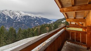 A wooden balcony with a view of snow-covered mountains and pine trees.