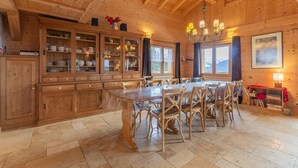 A wooden cabin interior with a dining table, chairs, cabinets, and a chandelier.