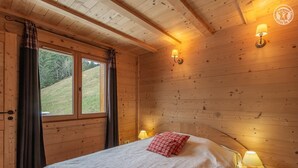 A wooden cabin bedroom with a bed, two bedside lamps, and a window with curtains.