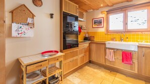 A kitchen with wooden cabinets, a black oven, a red bowl on a small table, and a window with a view of trees.