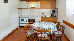 Una cocina compacta con zona de comedor, que incluye una mesa redonda con mantel floral, sillas de madera y electrodomésticos básicos como un microondas y una estufa.
