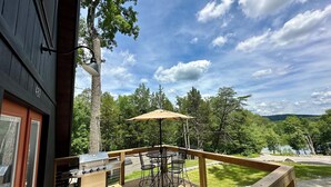 A wooden deck with a grill, outdoor table, and chairs, overlooking a forested area. - New Modern A-Frame Near Mammoth Cave National Park with Nolin Lake Views! (Cub Run)