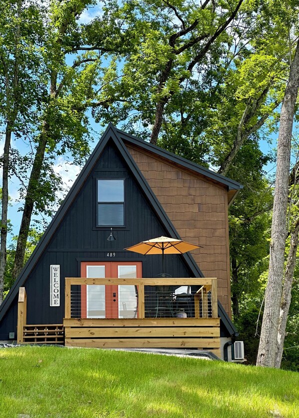 A cabin with a dark exterior, a wooden deck, a welcome sign, and a number 489. - New Modern A-Frame Near Mammoth Cave National Park with Nolin Lake Views! (Cub Run)