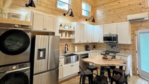 A modern kitchen with wooden paneling, stainless steel appliances, and a central island with bar stools. - New Modern A-Frame Near Mammoth Cave National Park with Nolin Lake Views! (Cub Run)