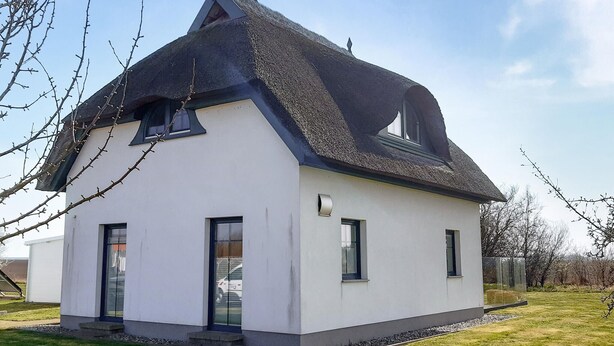 Ein modernes, zweistöckiges Haus mit einem steilen Satteldach, großen Fenstern und einer kleinen Veranda.