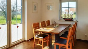 Ein Esszimmer mit Holztisch und -stühlen, großen Fenstern und Bildern an den Wänden.
