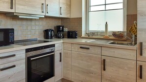 Eine moderne Küche mit Holzausstattung, Backofen, Mikrowelle, Kaffeemaschine und einem Fenster mit Jalousien.