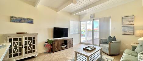 A spacious living room with a ceiling fan, a television, a green sofa, and a coffee table.