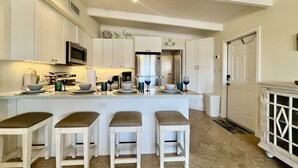 A modern kitchen with white cabinetry, a central island with stools, a microwave, and a stainless steel refrigerator. - DISCOUNT! Beautiful Home, Dock, Cabana Club Membership, Pool, Beach! (Key Colony Beach)
