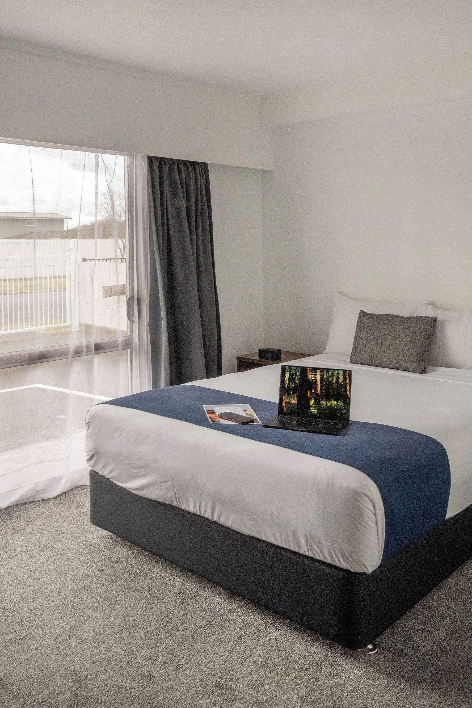 Une chambre d’hôtel avec un grand lit, une table de chevet, un ordinateur portable et une vue sur l’extérieur.
