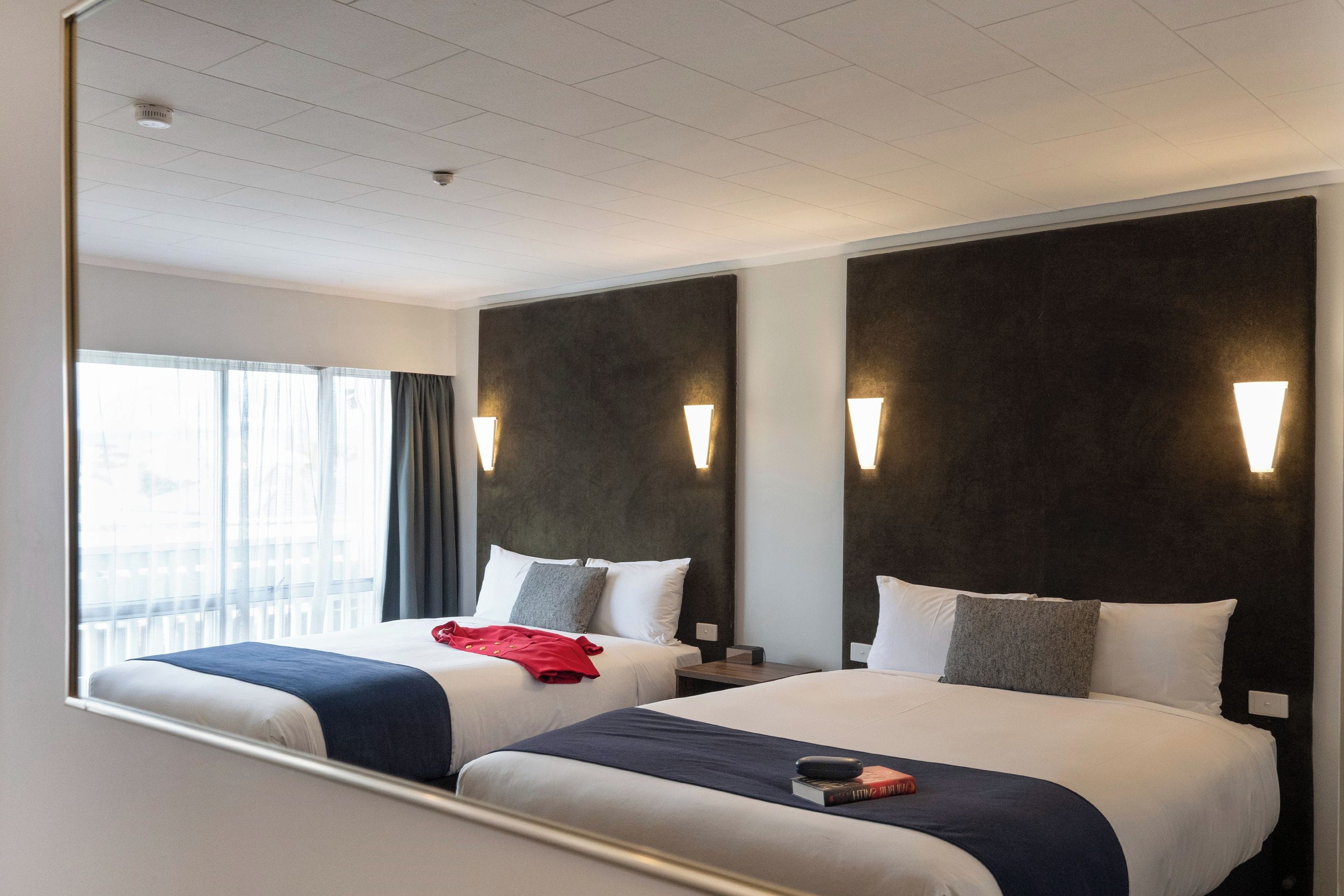 A hotel room with two beds, a large mirror, and a window with curtains.