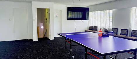 Una habitación con mesa de ping pong, televisión, sofá y puerta.