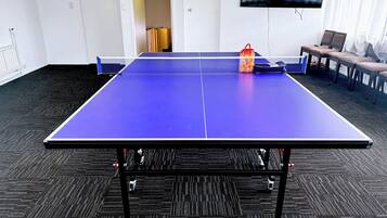 A ping pong table in a room with a carpeted floor, a TV on the wall, and a door marked 'STAFF ONLY'.