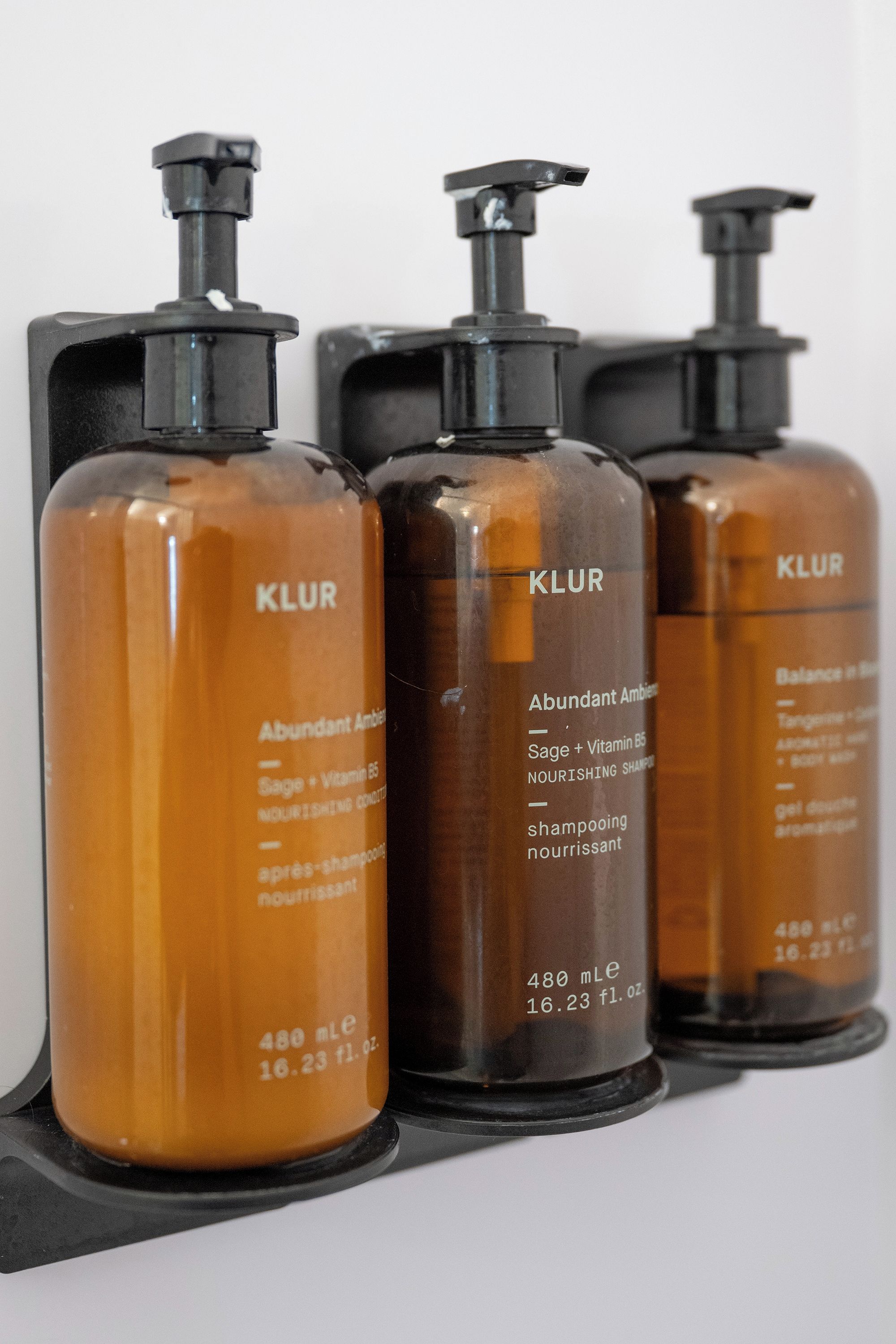 Tres botellas de champú KLUR con dispensadores bomba, cada una con ingredientes y beneficios diferentes indicados.