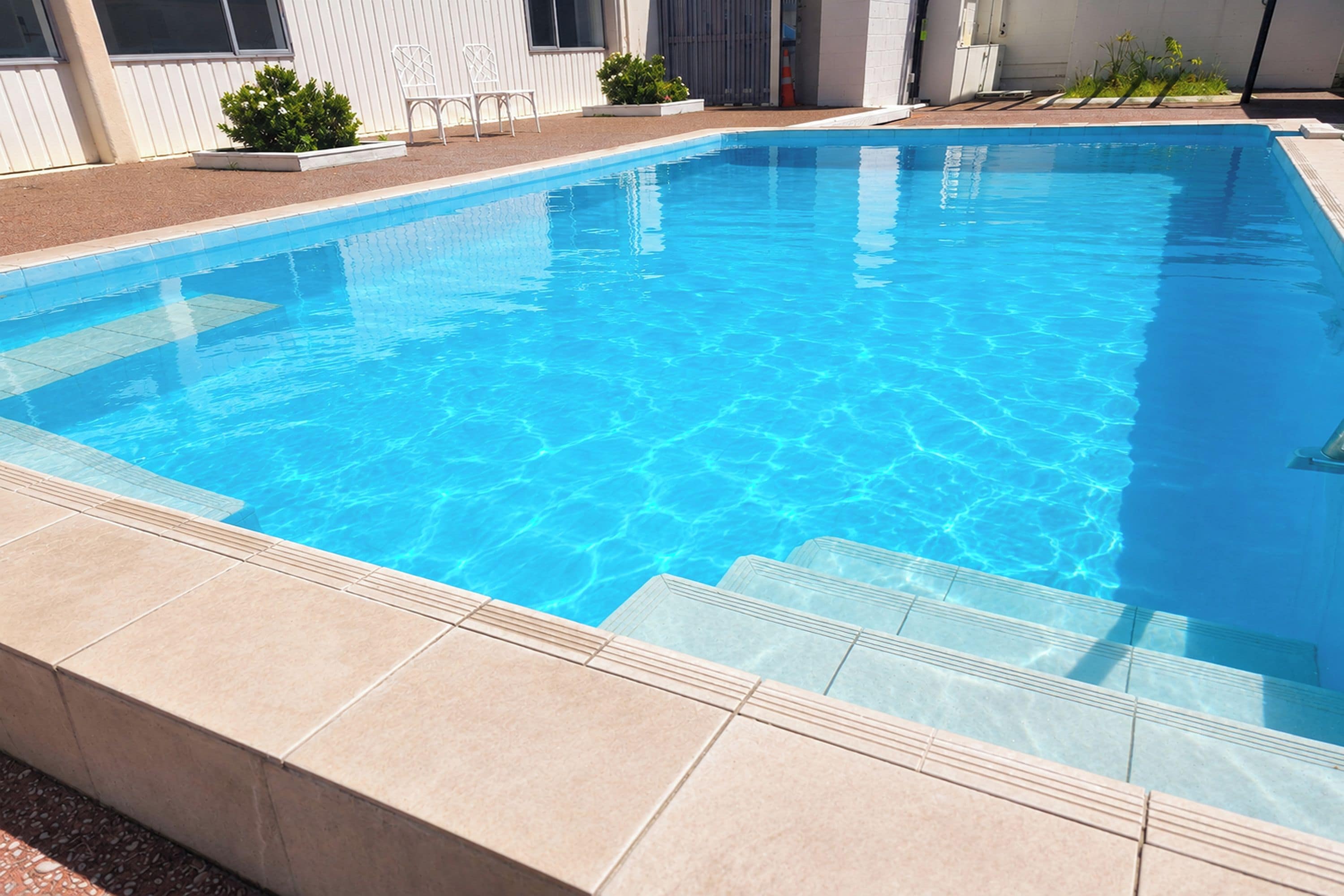 Una piscina rectangular con agua azul cristalina, rodeada por una solana con baldosas.