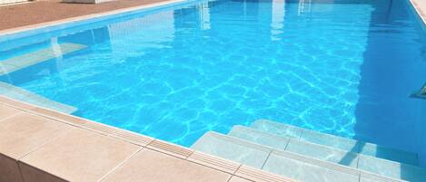 Una piscina rectangular con agua azul cristalina, rodeada por una solana con baldosas.