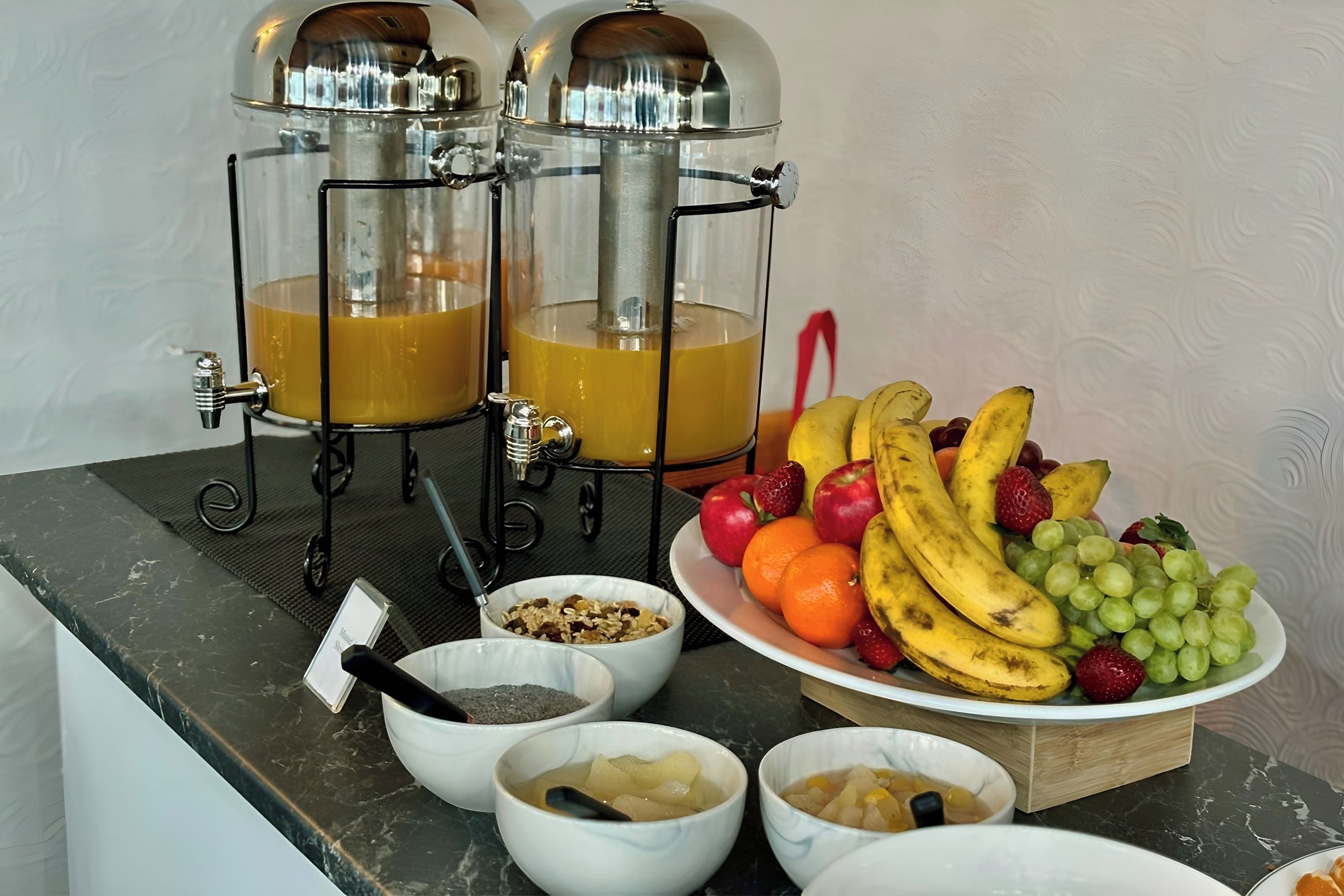 A breakfast setup with two juice dispensers, a fruit bowl, and bowls of cereal and yogurt.