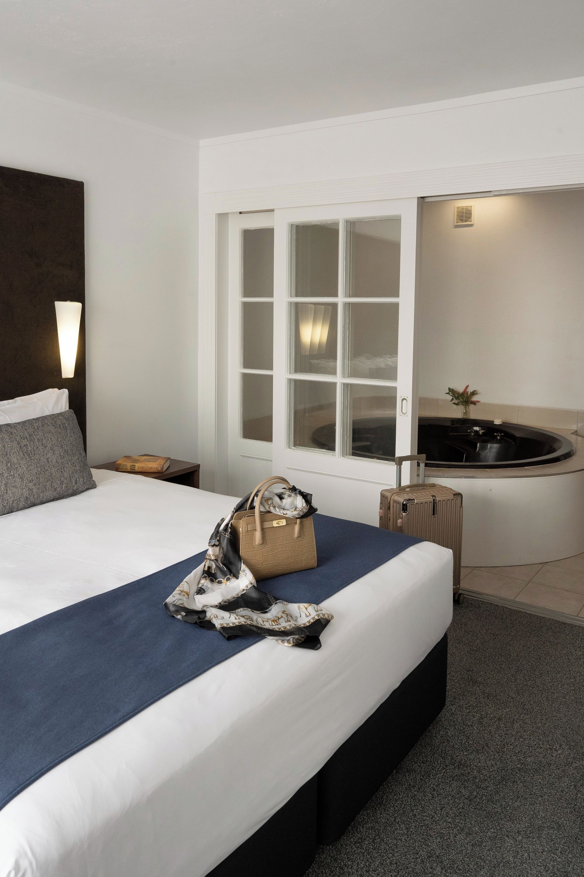 Una habitación de hotel con cama, ventana, baño y mesita de noche.