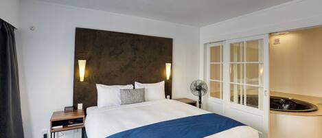 A hotel room with a bed, bedside table, lamp, and a window with a view.