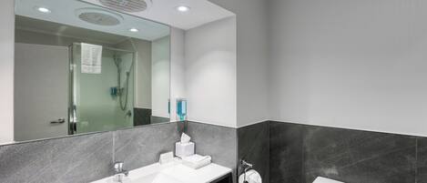 A modern bathroom with a white sink, dark tiled walls, a glass shower enclosure, and a toilet.