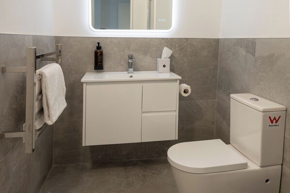 A modern bathroom with a toilet, a sink with a soap dispenser, a towel rack, and a toilet paper holder.