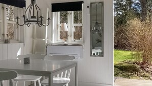Uma sala de jantar clara com uma mesa e cadeiras, um candelabro e vista para o exterior.