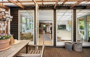 Una terraza de madera con una mesa, sillas, una cesta de mimbre y una planta en maceta.
