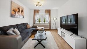 Un soggiorno moderno con un divano grigio scuro, un tavolino con un cesto in fibra naturale, una TV a schermo piatto e un quadro appeso al muro.