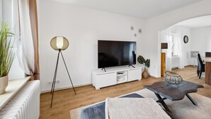 Un soggiorno moderno con una TV a schermo piatto, mobili bianchi, una lampada da terra e un'area pranzo sullo sfondo.