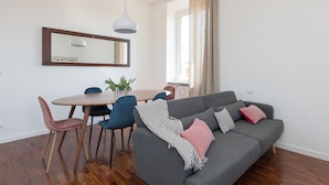 A modern living room with a grey sofa, a dining table with chairs, a potted plant, and a large window with curtains. - Penthouse with Terrace, Pantheon and 360° City views!! Walk to all attractions (Roma)